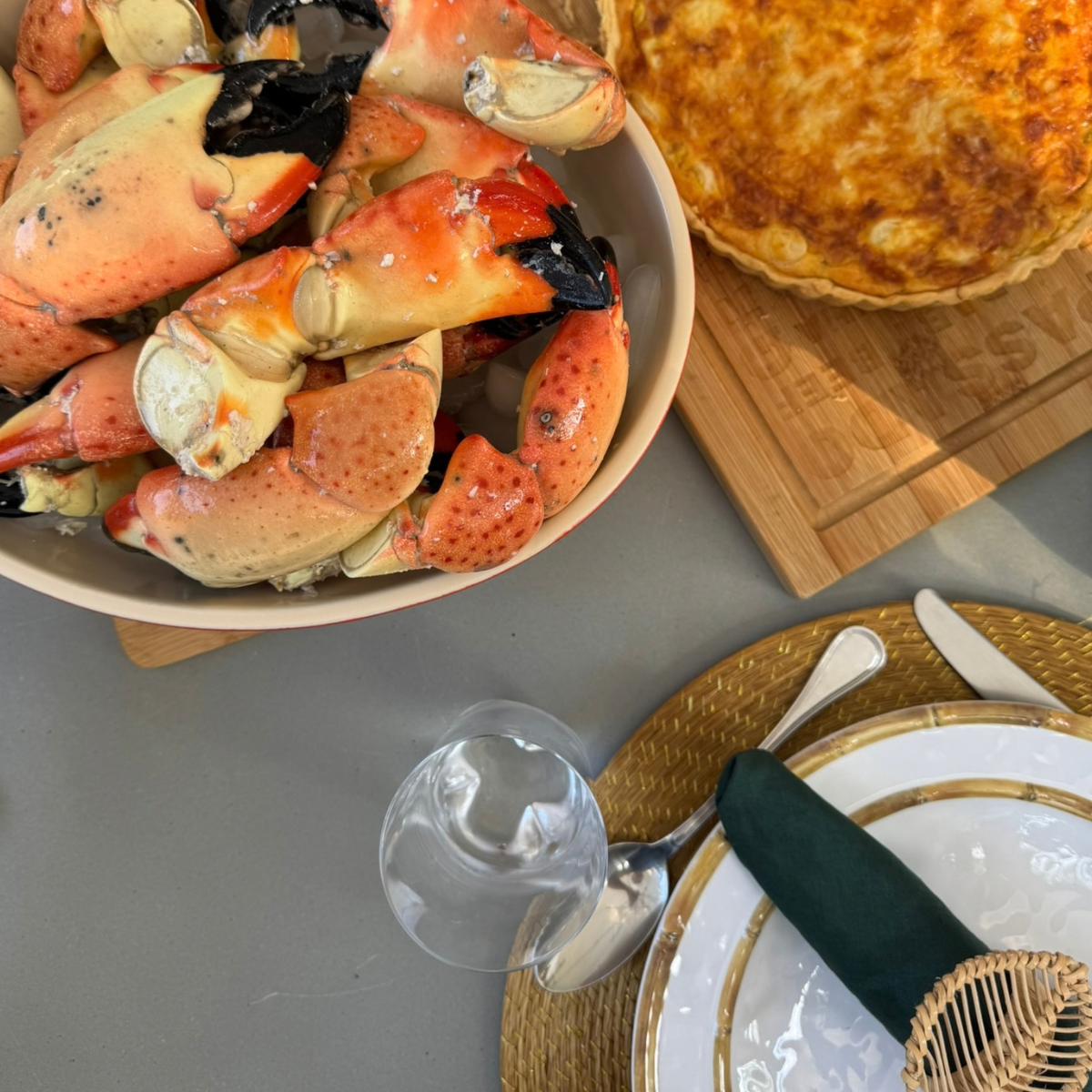 Stone crab claws in a bowl with a quiche next to it and a place setting nearby