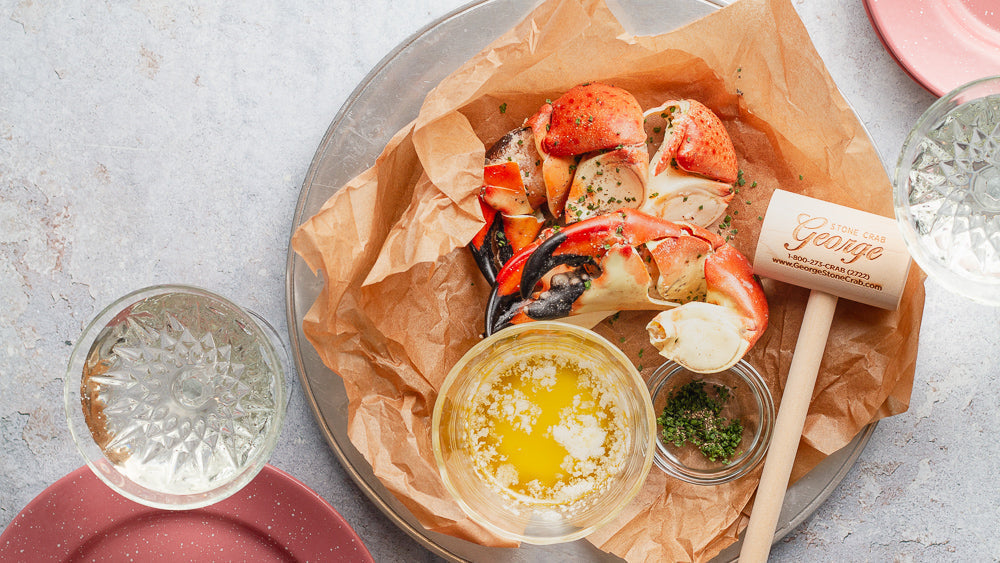 Stone crabs on a paper-lined plate with butter, herbs, and a George Stone Crab wooden mallet