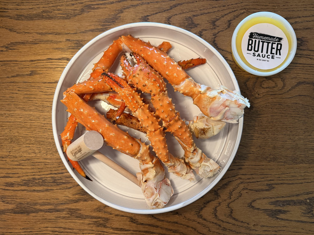 White plate with alaskan king crab legs and a container of butter sauce on a wooden surface.