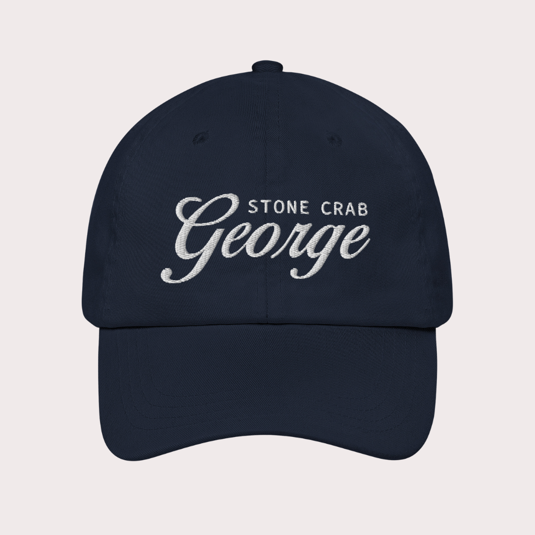 A navy blue baseball cap with white embroidered text reading 'STONE CRAB George' on the front, shown against a light gray background.